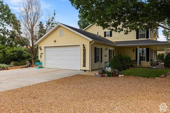 Yellow siding exterior with a two-car garage, concrete driveway, and a covered front porch