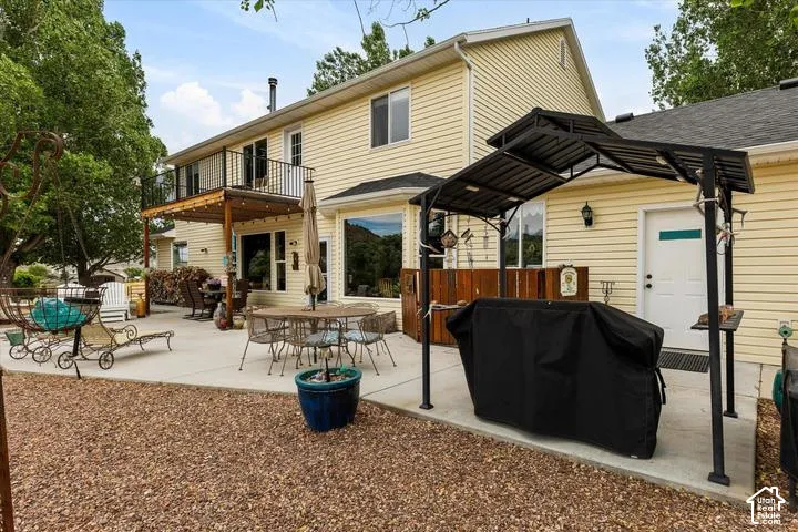 Expansive concrete patio with a detached gazebo frame, a built-in wooden bar area, and a second-story wooden deck with black metal railings