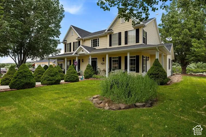 Two-story residence featuring light yellow siding, a covered front porch, black shutters, white columns, and a dark shingle roof