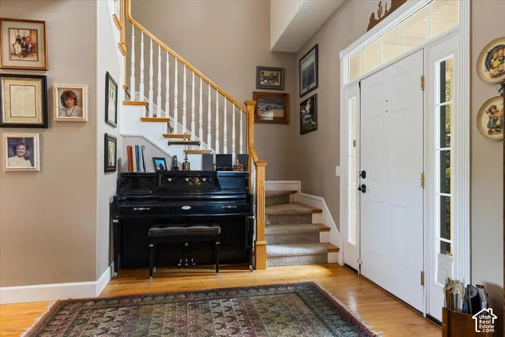 Entryway featuring hardwood flooring, a white paneled front door with sidelights and transom window, a carpeted staircase with white balusters and wood handrail, and neutral wall paint