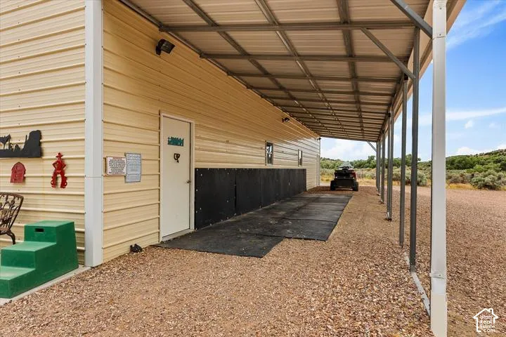 Metal-clad outbuilding featuring a covered gravel area, a secure entry door, wall-mounted exterior lighting, and a metal roof structure