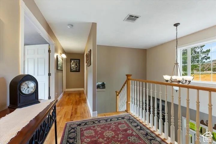 Upper-level landing featuring hardwood flooring, a white spindle staircase with a natural wood handrail, and a window with a natural landscape