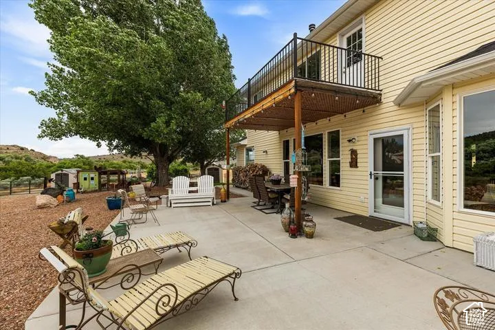 Spacious concrete patio with an overhead balcony featuring black metal railings and a shaded area with a slatted roof