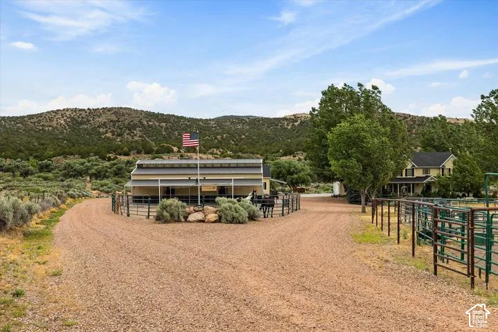 Gravel driveways leading to separate structures with fenced corrals and a backdrop of natural terrain