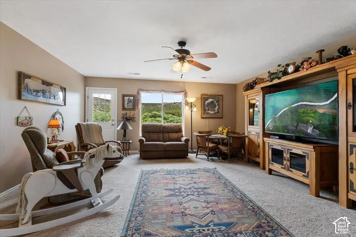 Spacious carpeted room featuring a ceiling fan with light fixture, multiple windows providing natural light, and a white paneled door