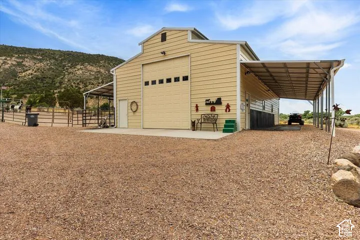 Cream-colored metal barn with a large garage door and attached covered carport, complemented by a fenced animal enclosure and a gravel-covered expanse