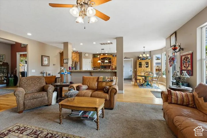 Open-concept living space featuring carpeted and wood-finish flooring, a ceiling fan with integrated lighting, and multiple windows