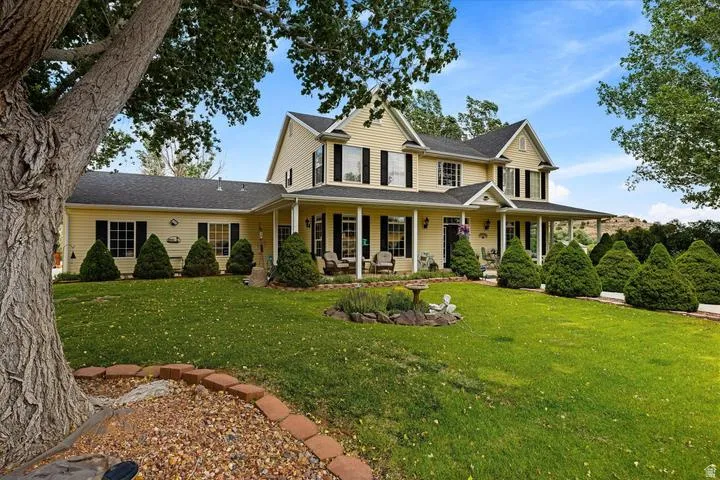 Yellow siding exterior featuring a covered porch, multiple dormer windows, and black window shutters