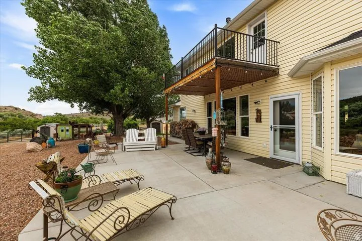 Spacious concrete patio with an overhead balcony featuring black metal railings and a shaded area with a slatted roof
