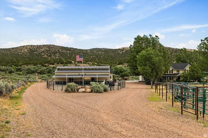 Gravel driveways leading to separate structures with fenced corrals and a backdrop of natural terrain