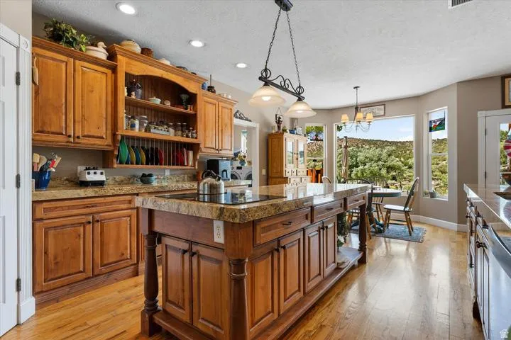 Spacious kitchen featuring custom wood cabinetry, granite countertops, a large center island with built-in cooktop, recessed lighting, and wood-finish flooring