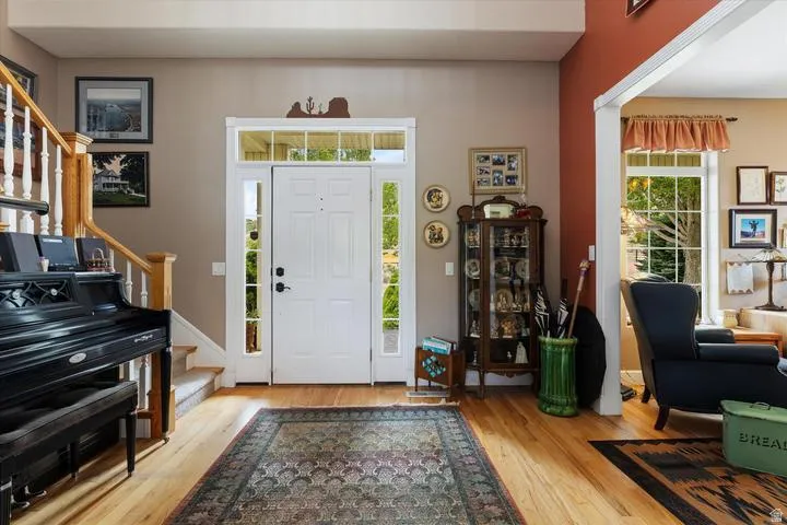 Entryway featuring a white paneled front door with sidelights and transom window, light wood-finish flooring, a staircase with wood banister and white spindles, and an arched opening to an additional room