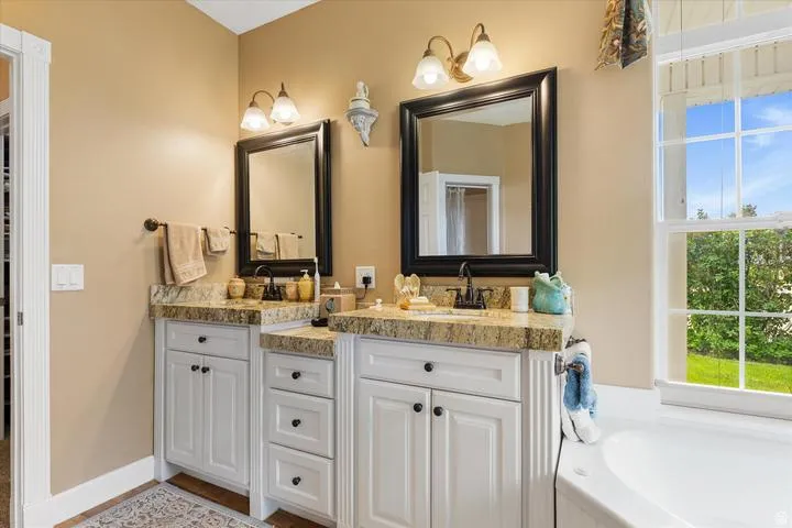 Dual vanity with granite countertops, white cabinetry, and individual framed mirrors