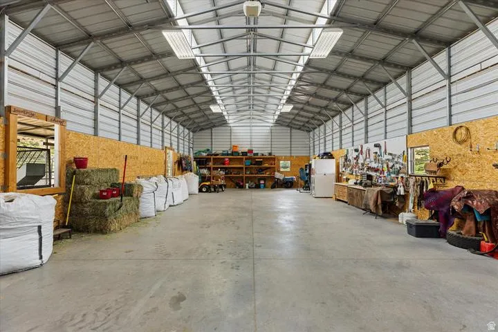Expansive metal-framed structure with a concrete floor, corrugated metal walls, and a vaulted ceiling featuring skylights