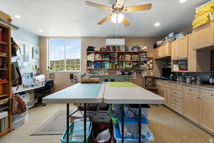 Spacious room featuring extensive built-in cabinetry with light wood-finish doors and drawers, a large window providing natural light, a ceiling fan, recessed lighting, and a wall-mounted air conditioning unit