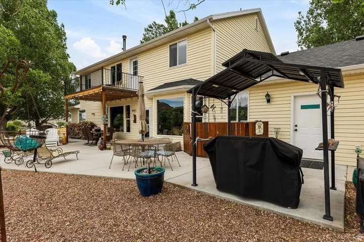 Expansive concrete patio with a detached gazebo frame, a built-in wooden bar area, and a second-story wooden deck with black metal railings