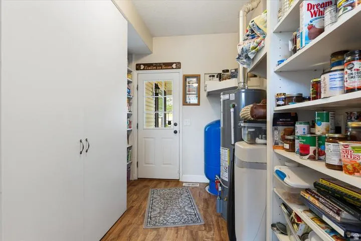 Utility room featuring wood-finish flooring, a white paneled door with glass inserts, and built-in white storage cabinets