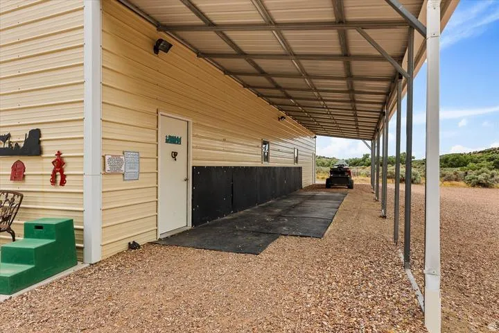 Metal-clad outbuilding featuring a covered gravel area, a secure entry door, wall-mounted exterior lighting, and a metal roof structure
