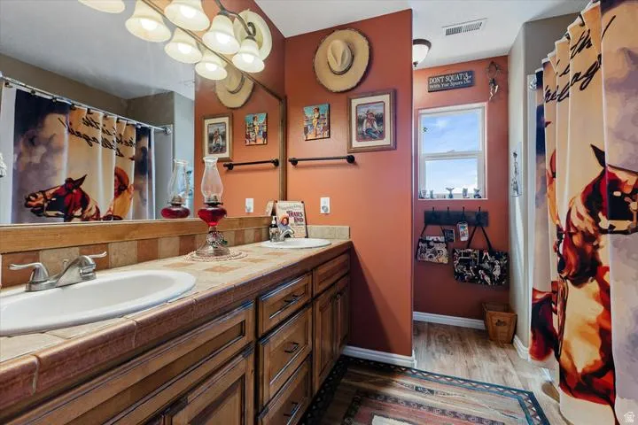 Bathroom featuring a dual vanity with tile countertop, wood-finish cabinetry, and an integrated mirror