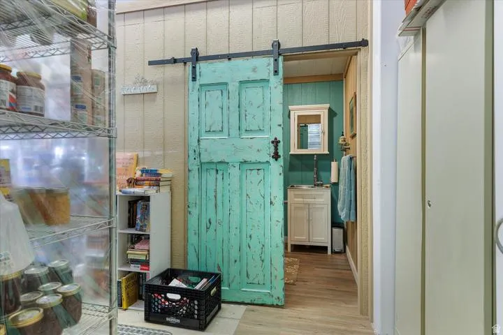 Distressed turquoise barn door with black hardware, opening to a space with vertical paneled walls and wood-finish flooring