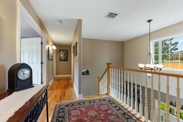 Upper-level landing featuring hardwood flooring, a white spindle staircase with a natural wood handrail, and a window with a natural landscape