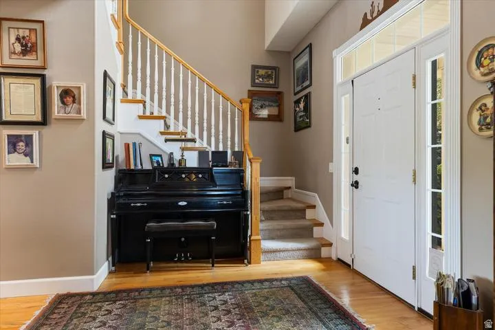 Entryway featuring hardwood flooring, a white paneled front door with sidelights and transom window, a carpeted staircase with white balusters and wood handrail, and neutral wall paint