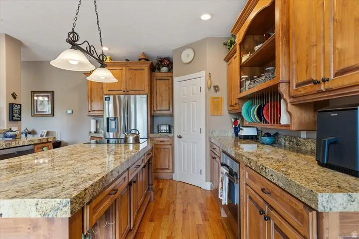 Kitchen featuring a large island with stone countertops, hardwood flooring, ample wood cabinetry, stainless steel refrigerator, and recessed lighting