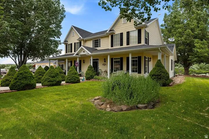 Two-story residence featuring light yellow siding, a covered front porch, black shutters, white columns, and a dark shingle roof