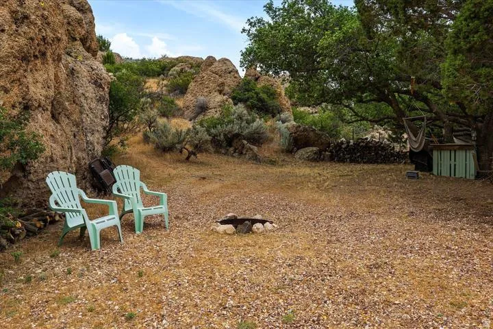 Outdoor gathering area featuring a stone-lined fire pit, natural rock formations, mature trees, and a gravel ground cover