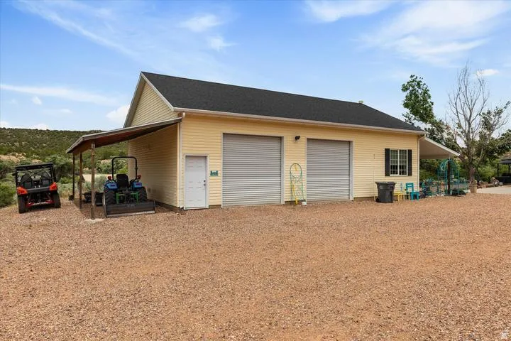 Detached garage featuring dual roll-up doors, a covered side patio, and a covered carport area