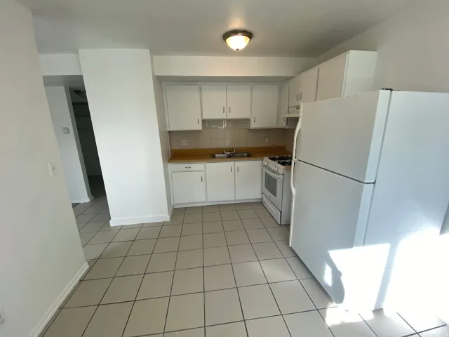 Kitchen featuring tile flooring, wood-finish countertops, white cabinetry, and a white appliance suite including a refrigerator, gas range, and microwave