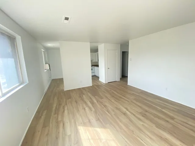 Spacious interior with wood-finish flooring, white walls, multiple windows, and a white interior door