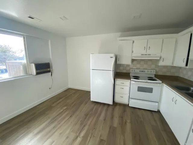Kitchen area featuring wood-finish flooring, white cabinetry with matching appliances, a double basin sink, and a tiled backsplash