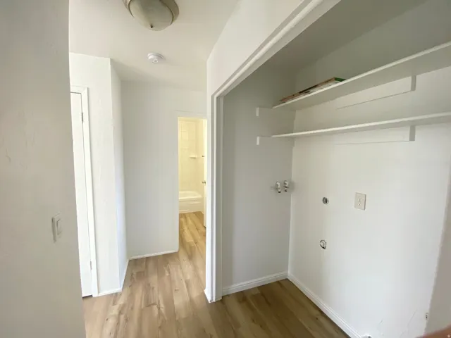Laundry area featuring wood-finish flooring, white walls, built-in shelving, and utility hookups