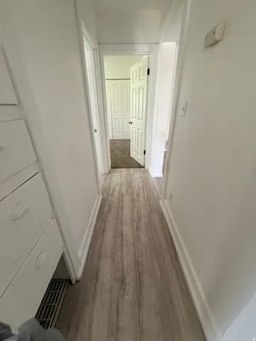Hallway featuring wood-finish flooring, white baseboards, and white walls
