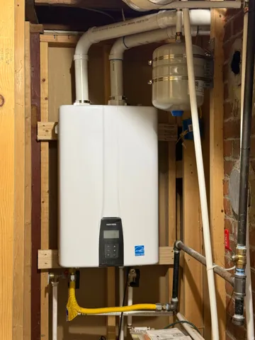 Wall-mounted tankless water heater with digital display, connected to PVC piping and a pressure expansion tank
