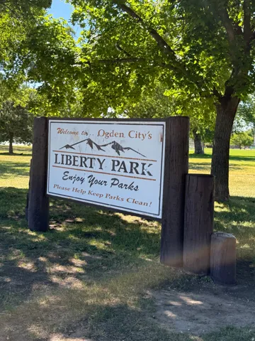 Wood-framed park signage featuring a white display board with "Ogden City's Liberty Park" text