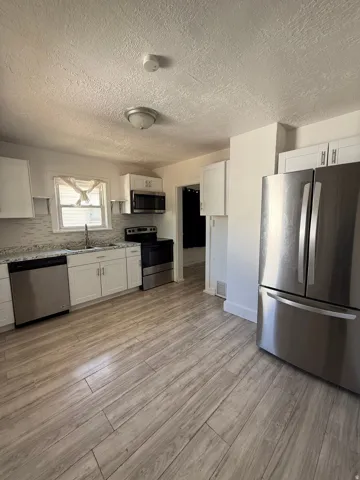 Contemporary kitchen featuring stainless steel appliances, white cabinetry, wood-finish flooring, light-toned countertops, and a tiled backsplash