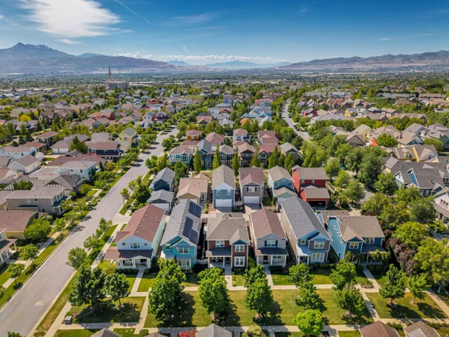 Expansive aerial perspective showcasing a residential community with diverse home styles, tree-lined streets, and distant mountain backdrops