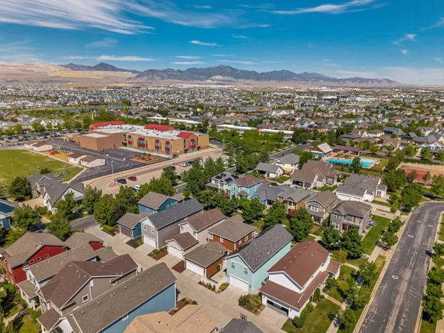 Aerial perspective showcasing a residential neighborhood with varied single-family homes, a prominent educational facility with playground and athletic field, an outdoor swimming pool, and a tennis court