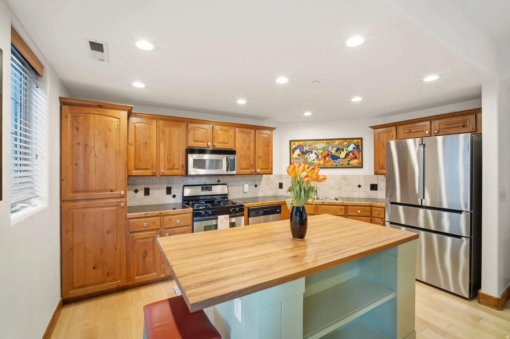 Kitchen with wood-finish cabinetry, stainless steel appliances, and a central island featuring a light wood countertop