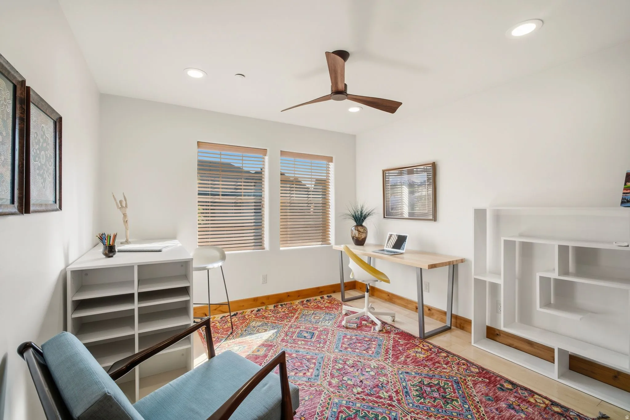 Recessed lighting illuminates this bright room featuring two windows with blinds, a ceiling fan with wood-finish blades, and wood baseboard trim