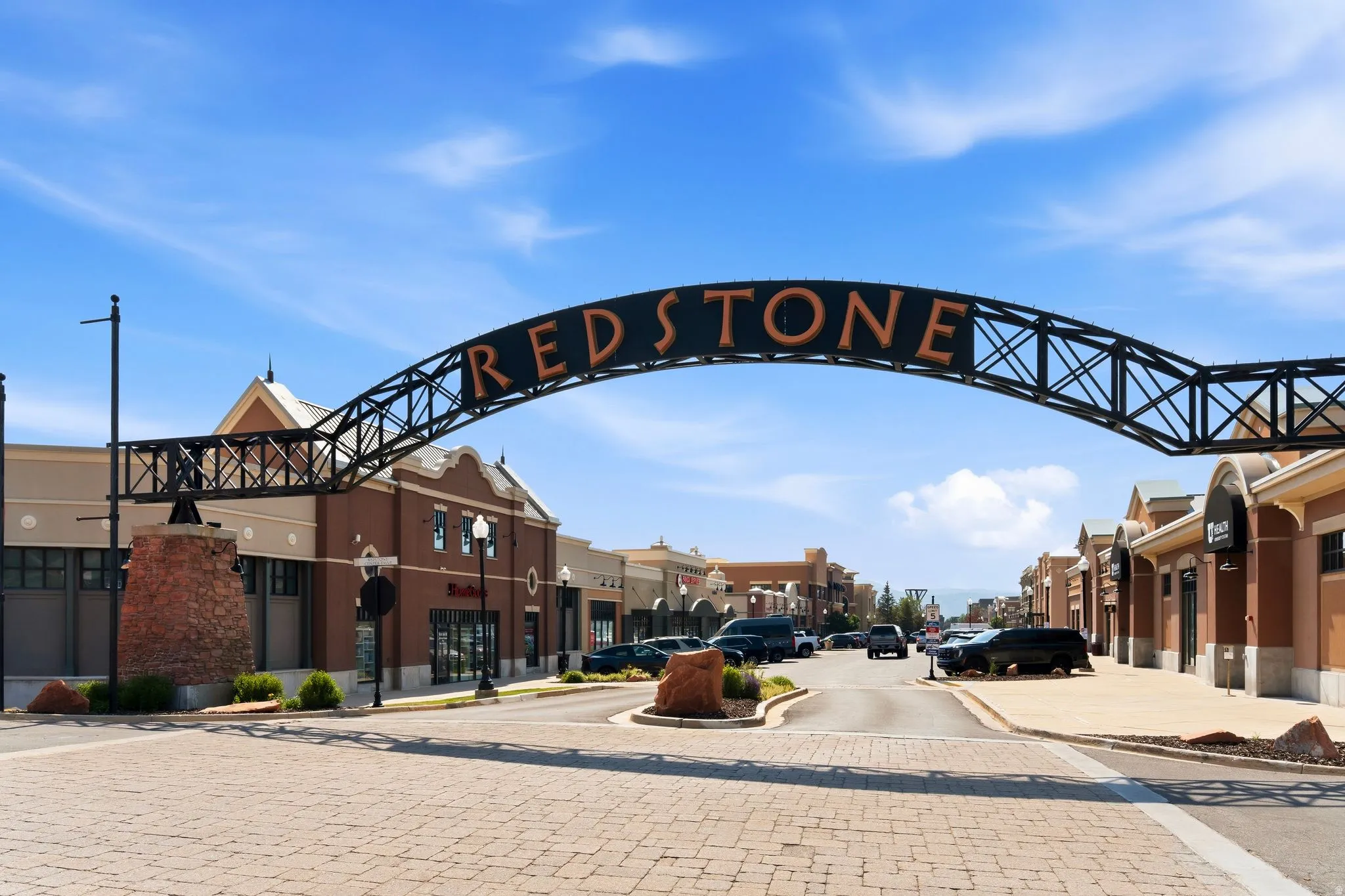 Redstone entry archway over a paver road, flanked by commercial buildings featuring brick and stucco facades with storefront windows