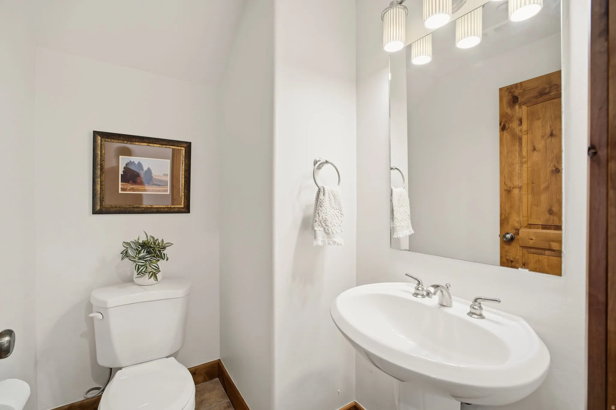 Pedestal sink with chrome fixtures, framed mirror, and contemporary vanity lighting