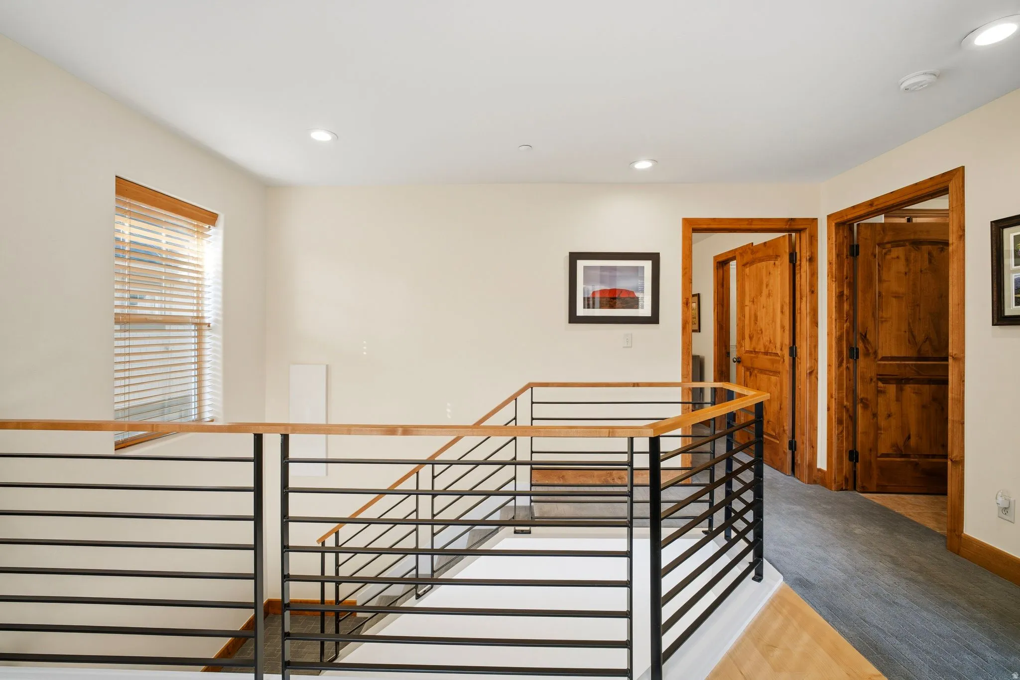 Upper level landing featuring modern railing with metal spindles and a wood-finish handrail, recessed lighting, and wood-finish doors