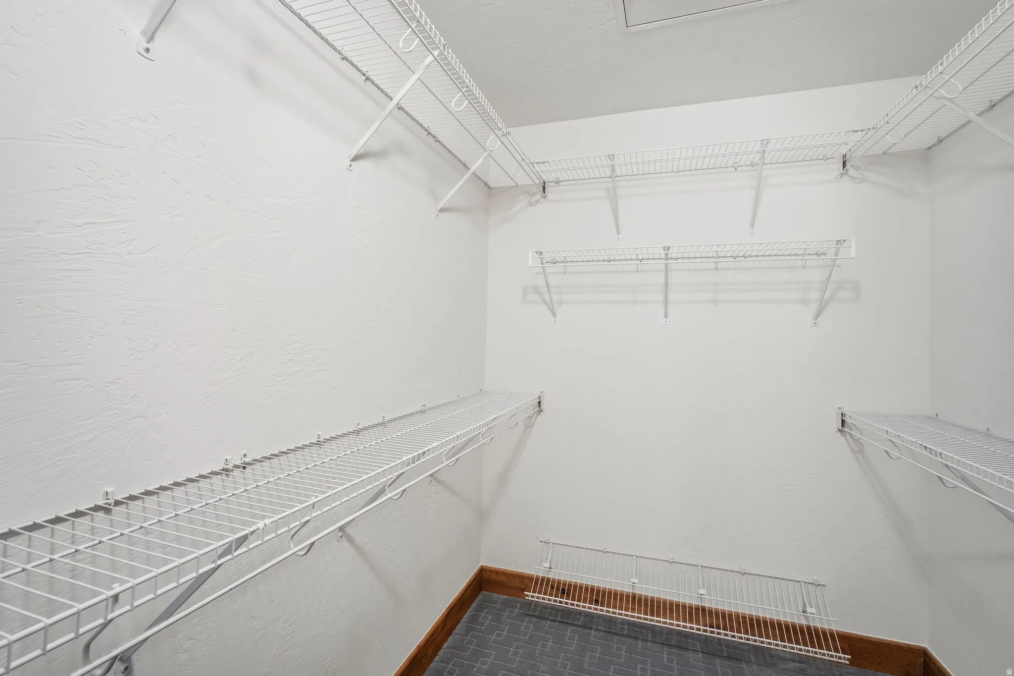 Walk-in closet featuring extensive wire shelving, white textured walls, and a durable tile-style flooring with perimeter wood-finish trim