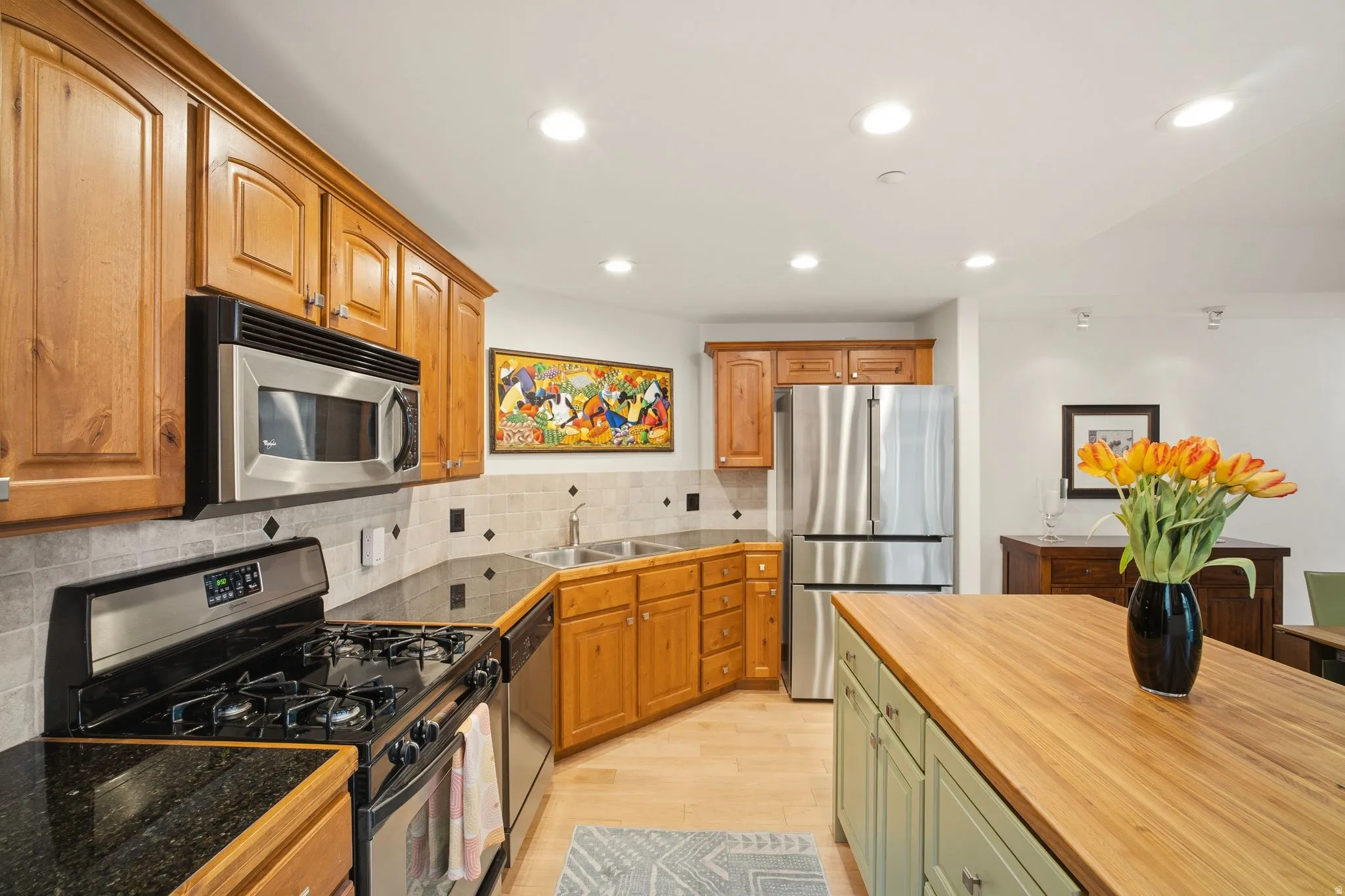 Kitchen featuring light wood cabinetry, stainless steel appliances, dark stone countertops, and a light-toned tile backsplash