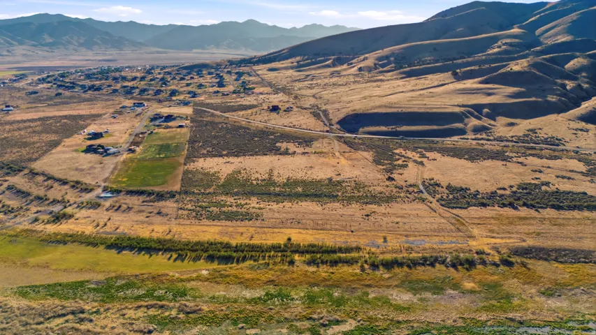 Expansive rural landscape featuring distant residential properties, natural terrain, and prominent mountain ranges