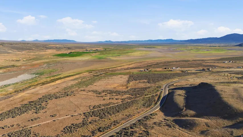 Expansive undeveloped land featuring varied terrain, a paved road, natural vegetation, and distant mountain ranges