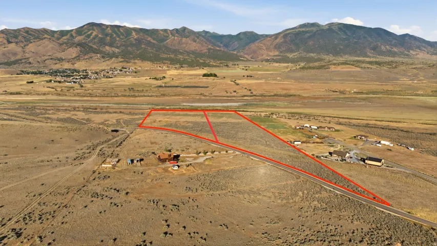 Expansive undeveloped land parcel outlined in red, featuring natural vegetation, a distant mountain range, and scattered residences